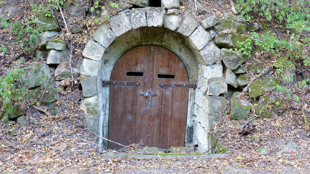 In einen Hügel ist ein gemauerter Torbogen mit einer kleinen hölzernen Tür eingelassen. 