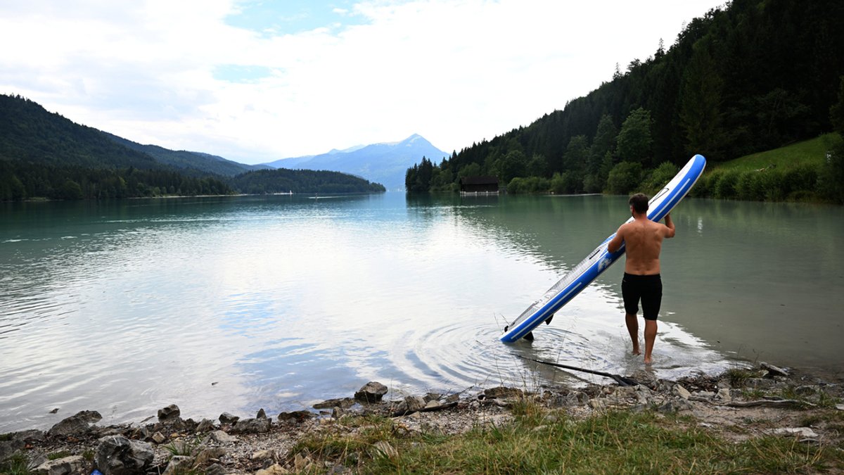 Ein Stand-Up-Paddler bringt in Niedernach sein Brett ins Wasser des Walchensee.