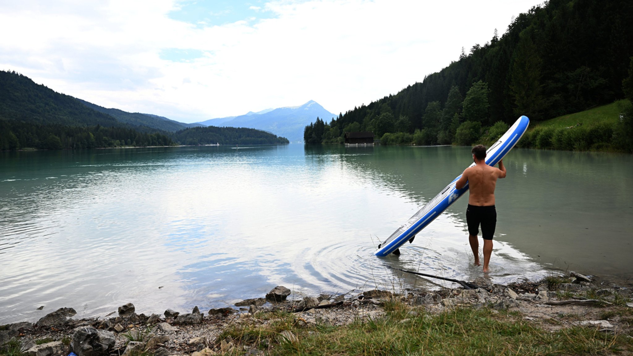 Ein Stand-Up-Paddler bringt in Niedernach sein Brett ins Wasser des Walchensee.