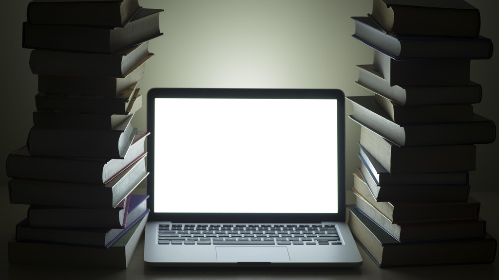Ein Laptop zwischen Bücherstapel (Symbolbild)