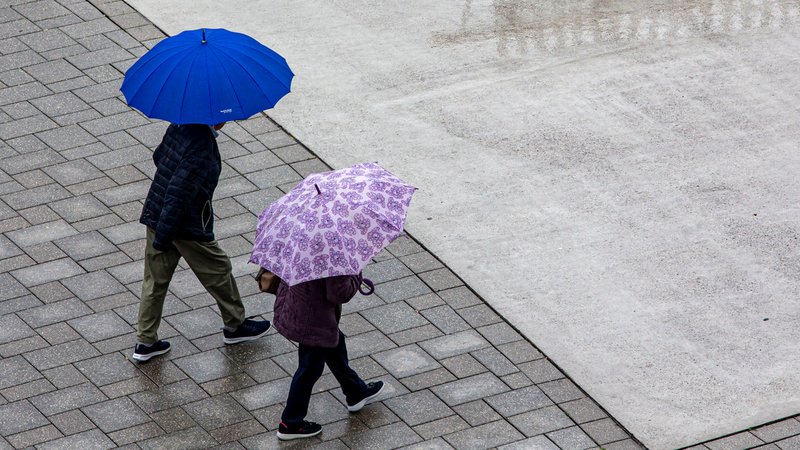 Zwei Menschen mit Regenschirmen gehen auf einem Platz nebeneinander. | Bild: pa/Goldmann Zwei Menschen mit Regenschirmen gehen auf einem Platz nebeneinander.