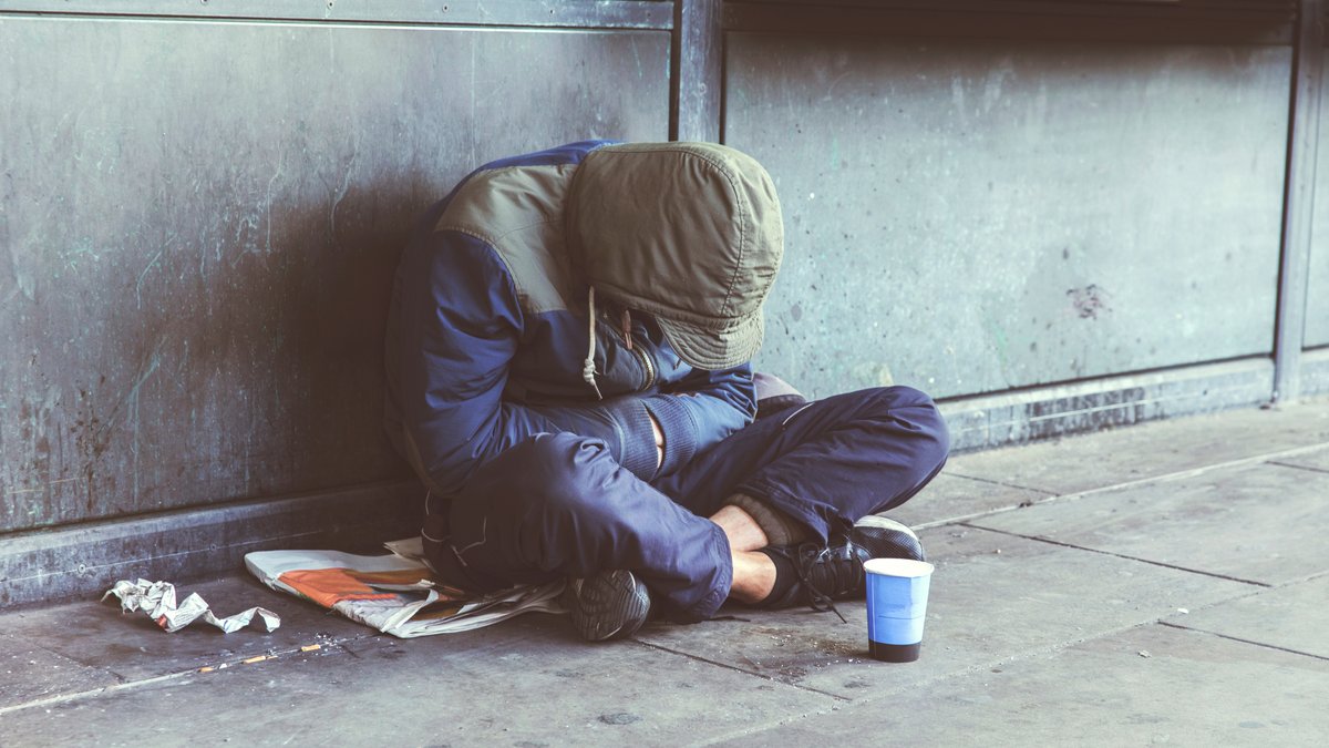 Ein junger Mann sitzt als Obdachloser am Boden auf dem Gehweg. Wenn es Zuhause unerträglich wird, wissen viele Jugendliche nicht wohin. (Symbolbild)