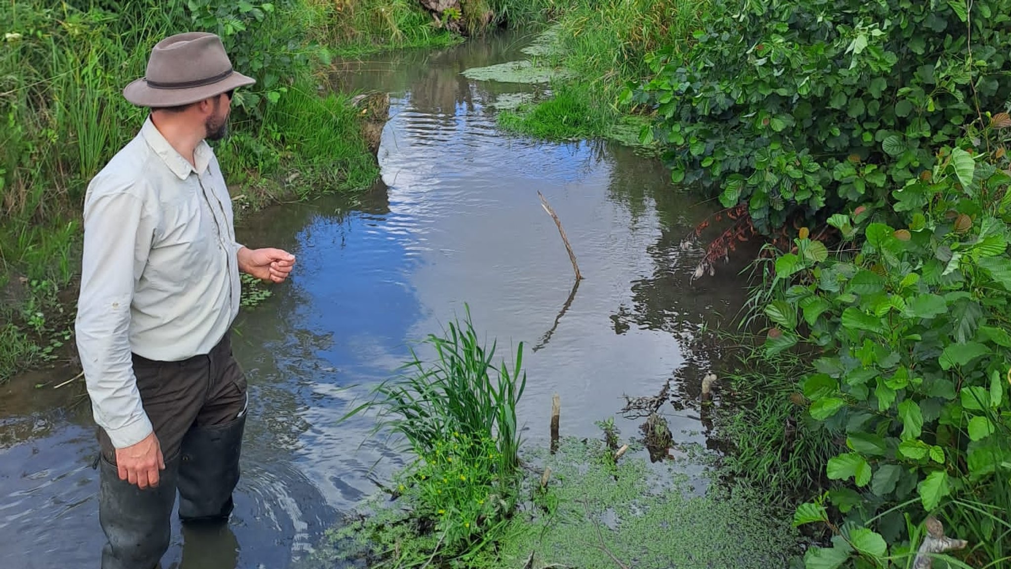 Mann mit Hut steht in einem kleinen Bach und schaut dem Wasser nach