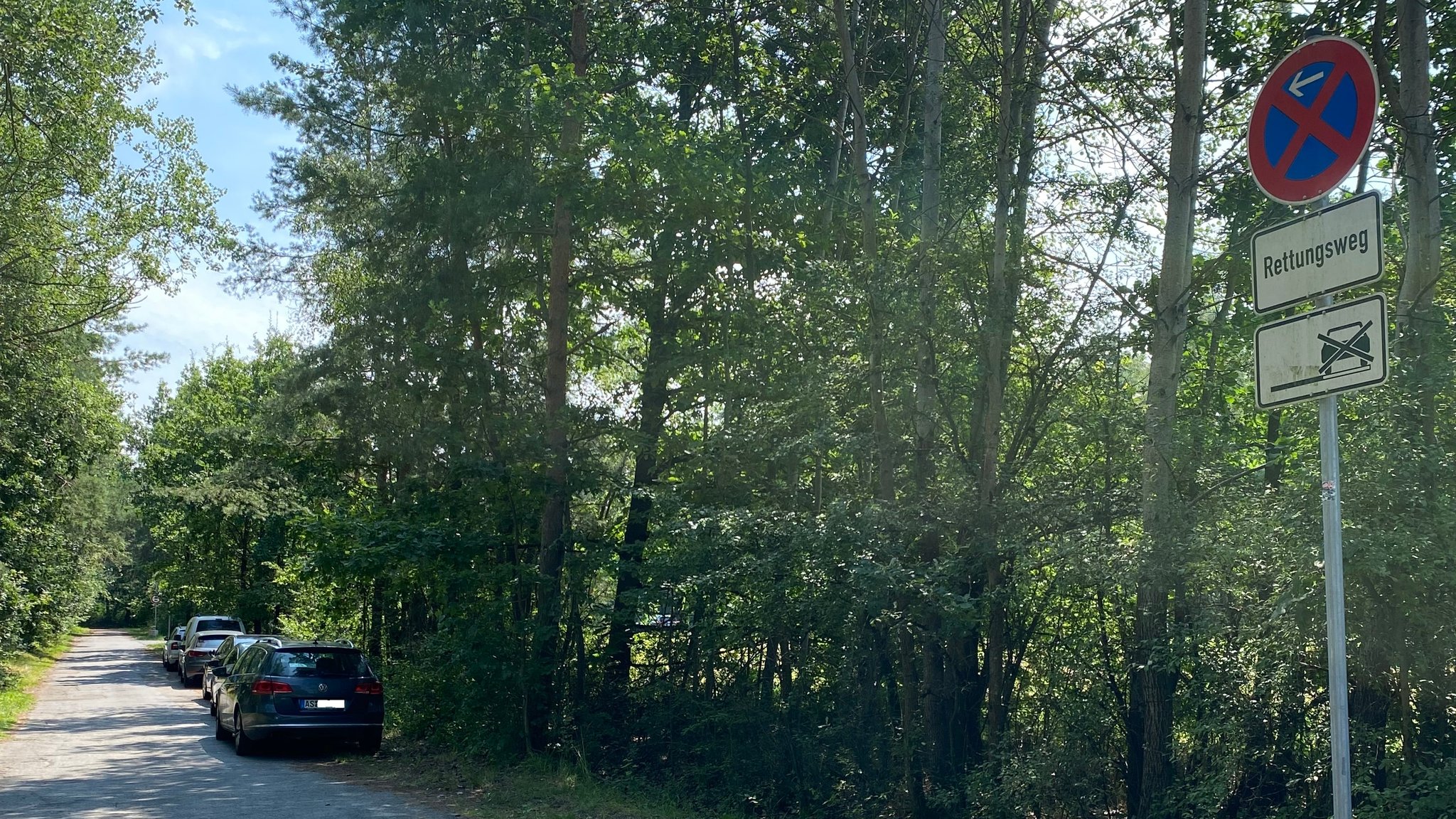 Autos stehen geparkt an einer schmalen Straße, ein Schild verweist auf einen Rettungsweg.