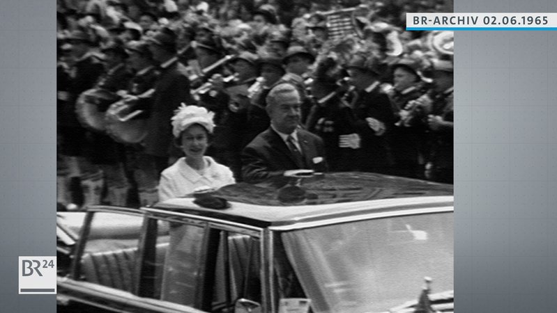 Königin Elisabeth II. im offenen Wagen stehend