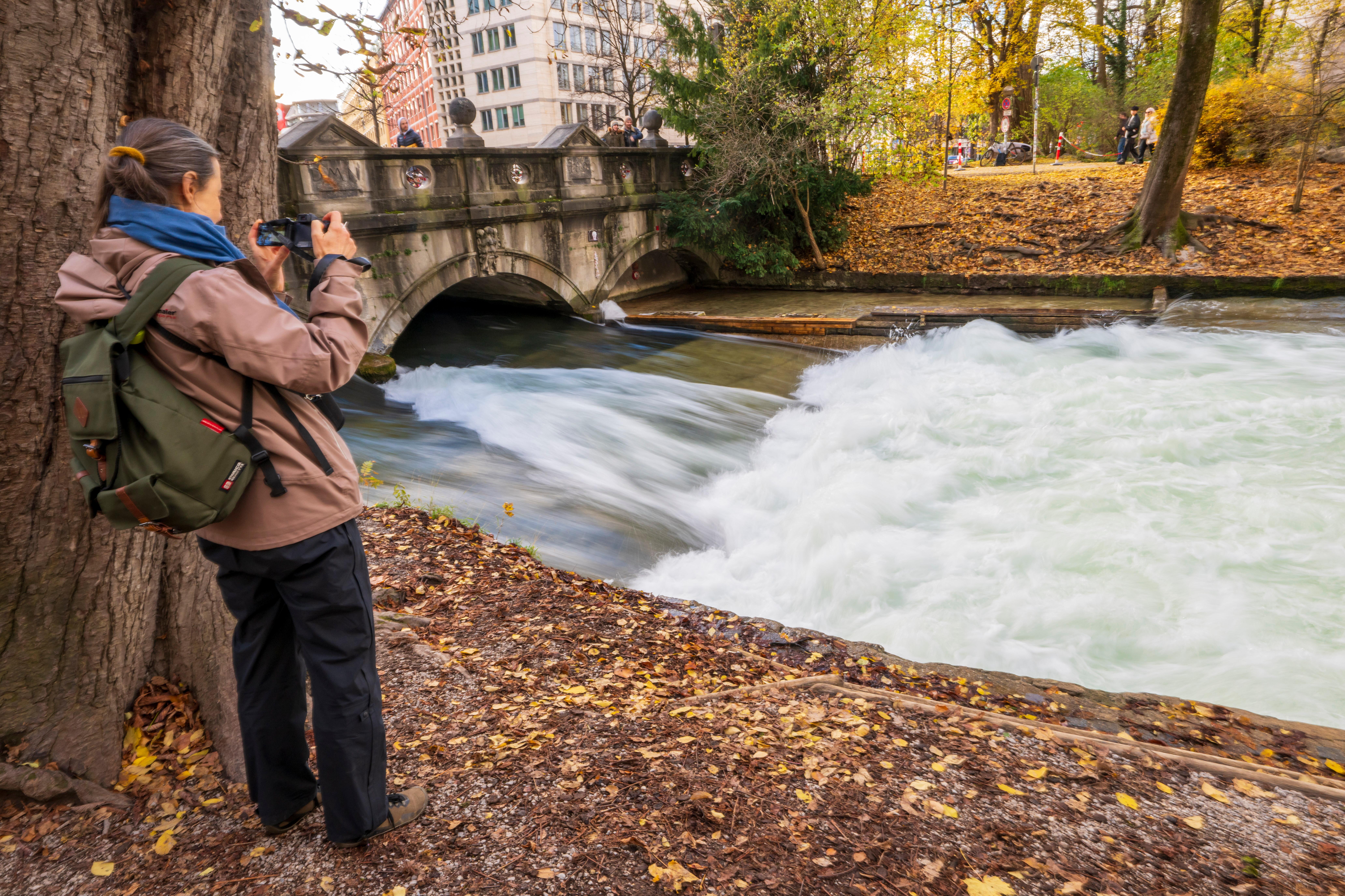 Eine Frau filmt die Stelle am Rande des Englischen Garten, an der sich normalerweise die Eisbachwelle bildet. Diese ist aktuell verschwunden. Surfen ist momentan nicht möglich. Die Eisbachwelle ist sonst zu jeder Jahres- und Tageszeit ein wahrer Hotspot für Touristen und Surfer aus der ganzen Welt. Foto vom 02.11.2025.