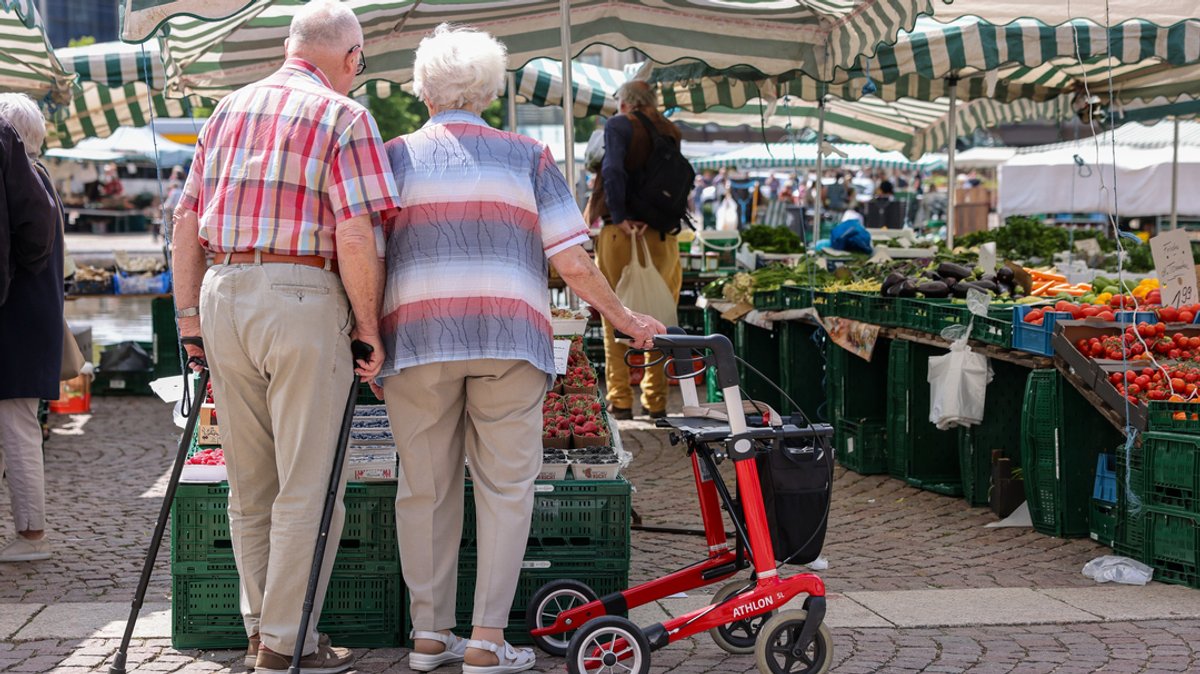 Zwei Senioren stehen mit Gehhilfen und Rollator auf dem Wochenmarkt in der Leipziger Innenstadt.