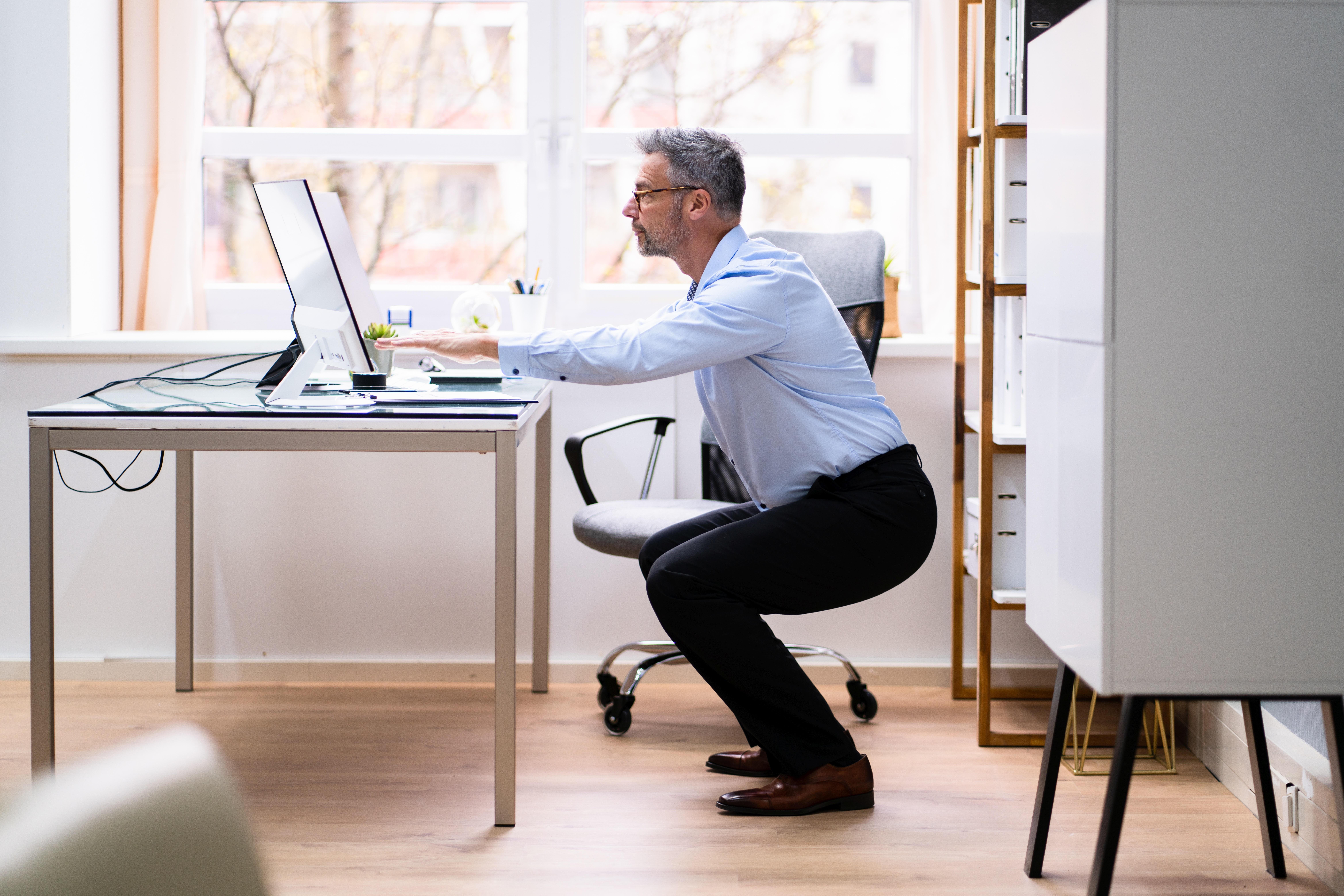 Mann am Schreibtisch macht Kniebeugen