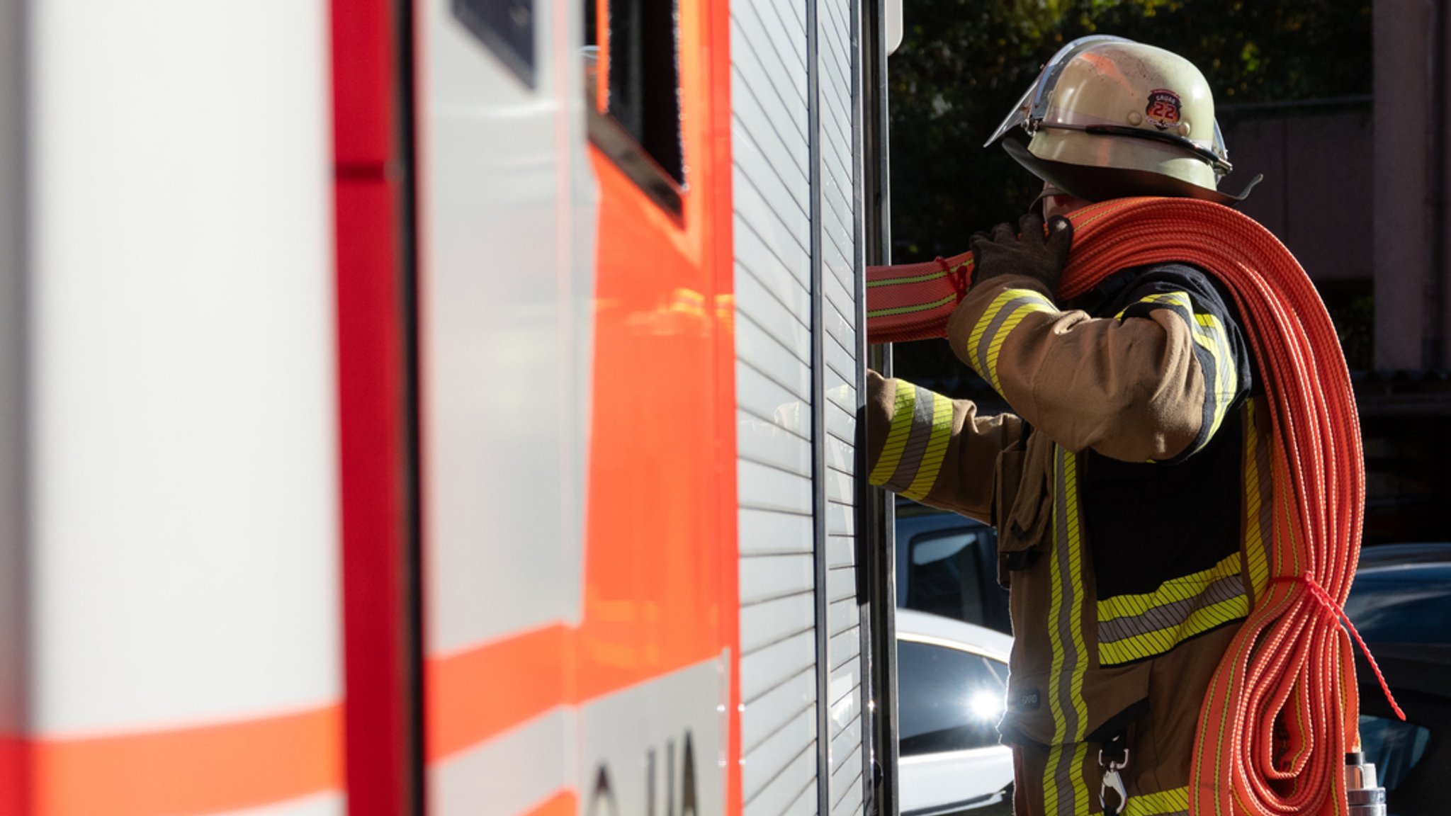 Feuerwehrmann hat Schlauch über der Schulter, steht neben einem Feuerwehrauto