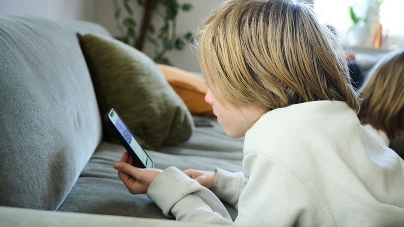 (Symbolbild) Ein Junge liegt auf einem Sofa und guckt auf sein Smartphone. | Bild: dpa-Bildfunk/Annette Riedl (Symbolbild) Ein Junge liegt auf einem Sofa und guckt auf sein Smartphone.