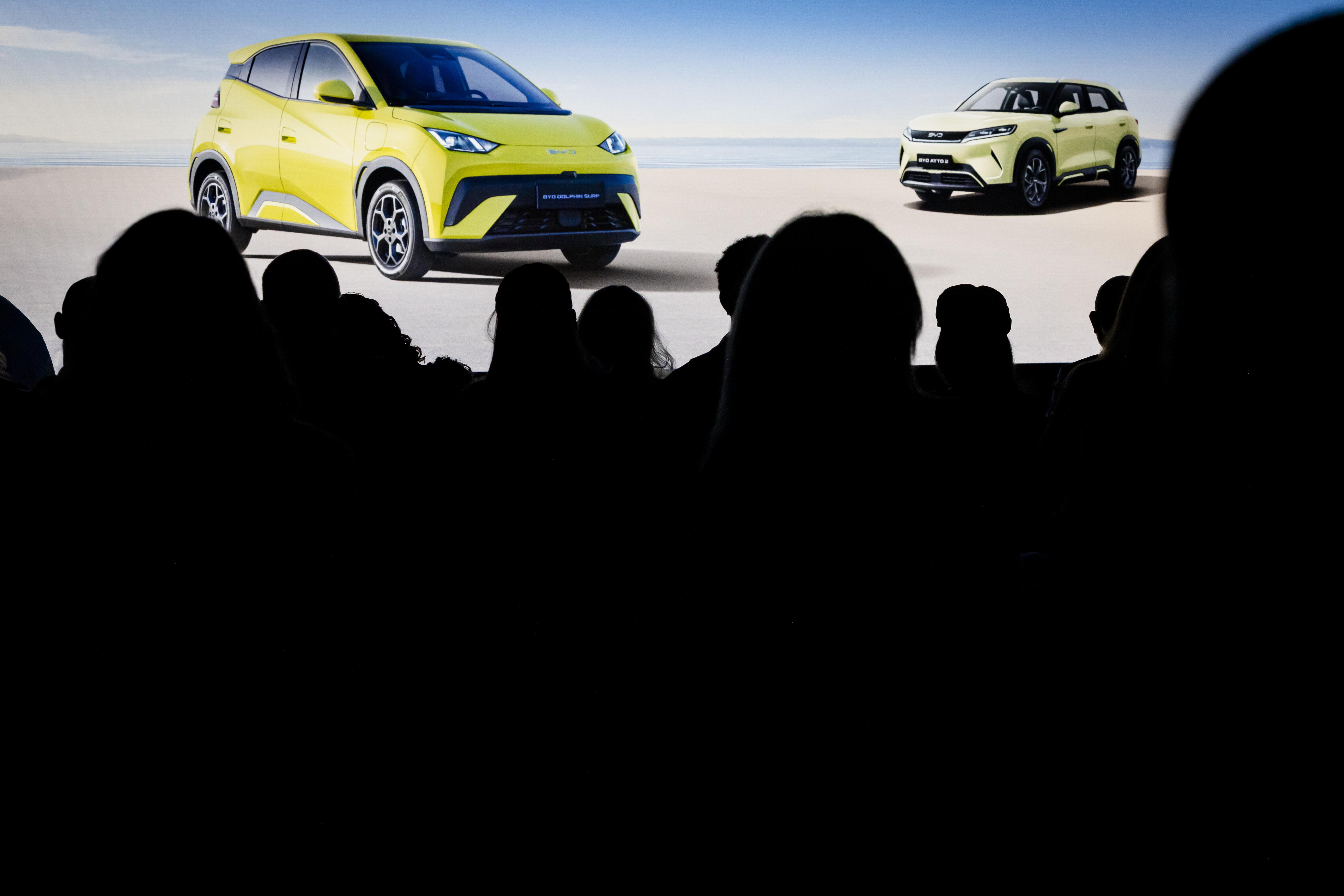 Auf einem Bildschirm ist der gelbe Kleinwagen "Dolphin Surf" zu sehen, davor Silhouette der Köpfe von IAA Mobility-Besuchern