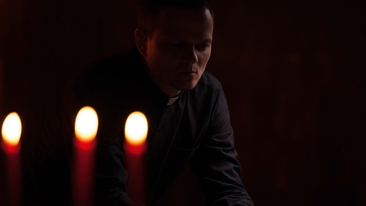 Priester im Dunkeln mit drei Kerzen im Vordergrund