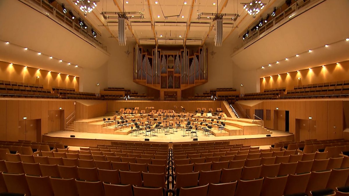 Ein fensterloser Konzertsaal mit leeren Stuhlreihen und der Bühne, auf der Stühle stehen.