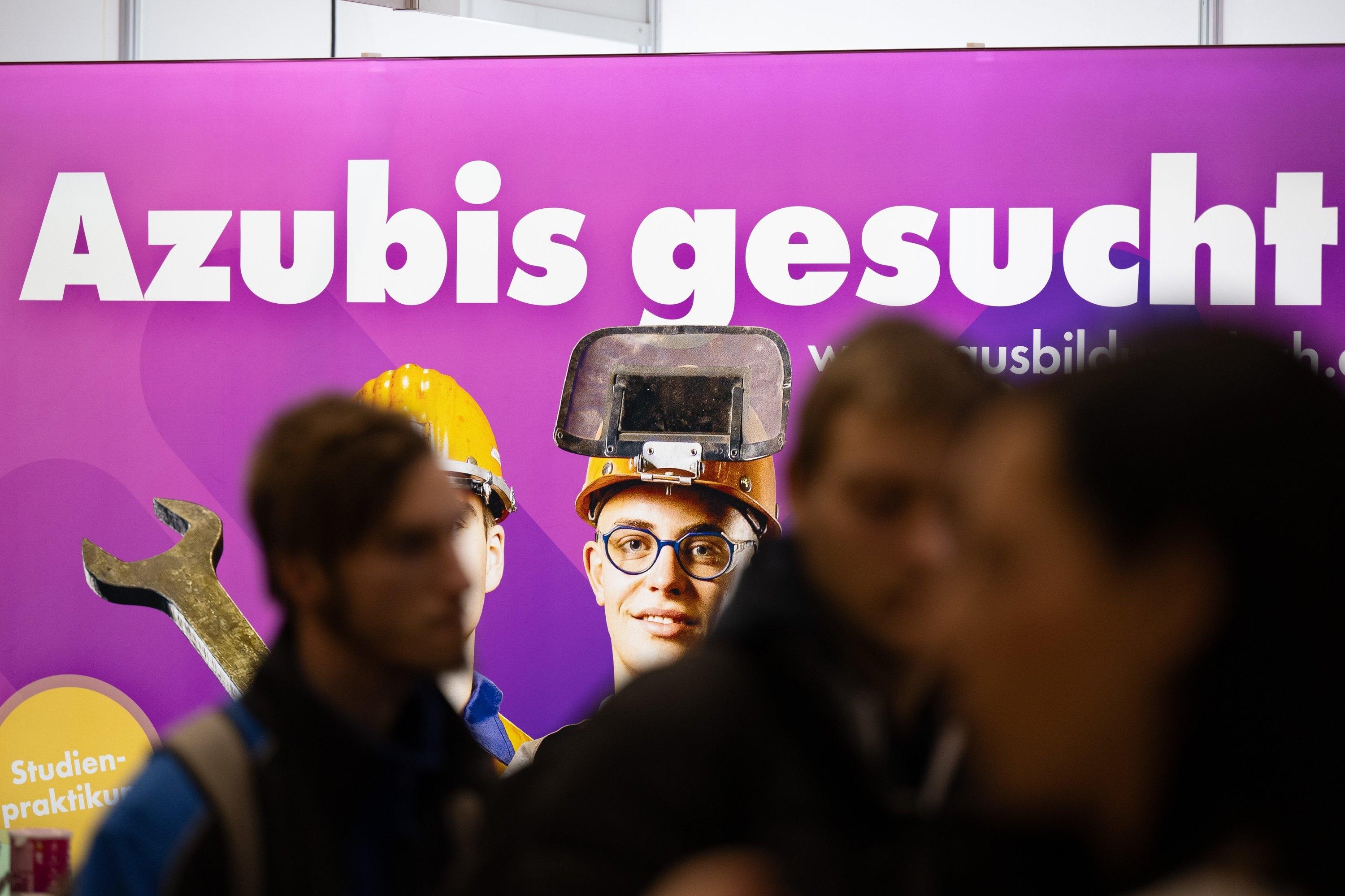 Besucher stehen auf einer Jobmesse vor einem Plakat mit dem Schriftzug "Azubis gesucht" (Symbolbild). 