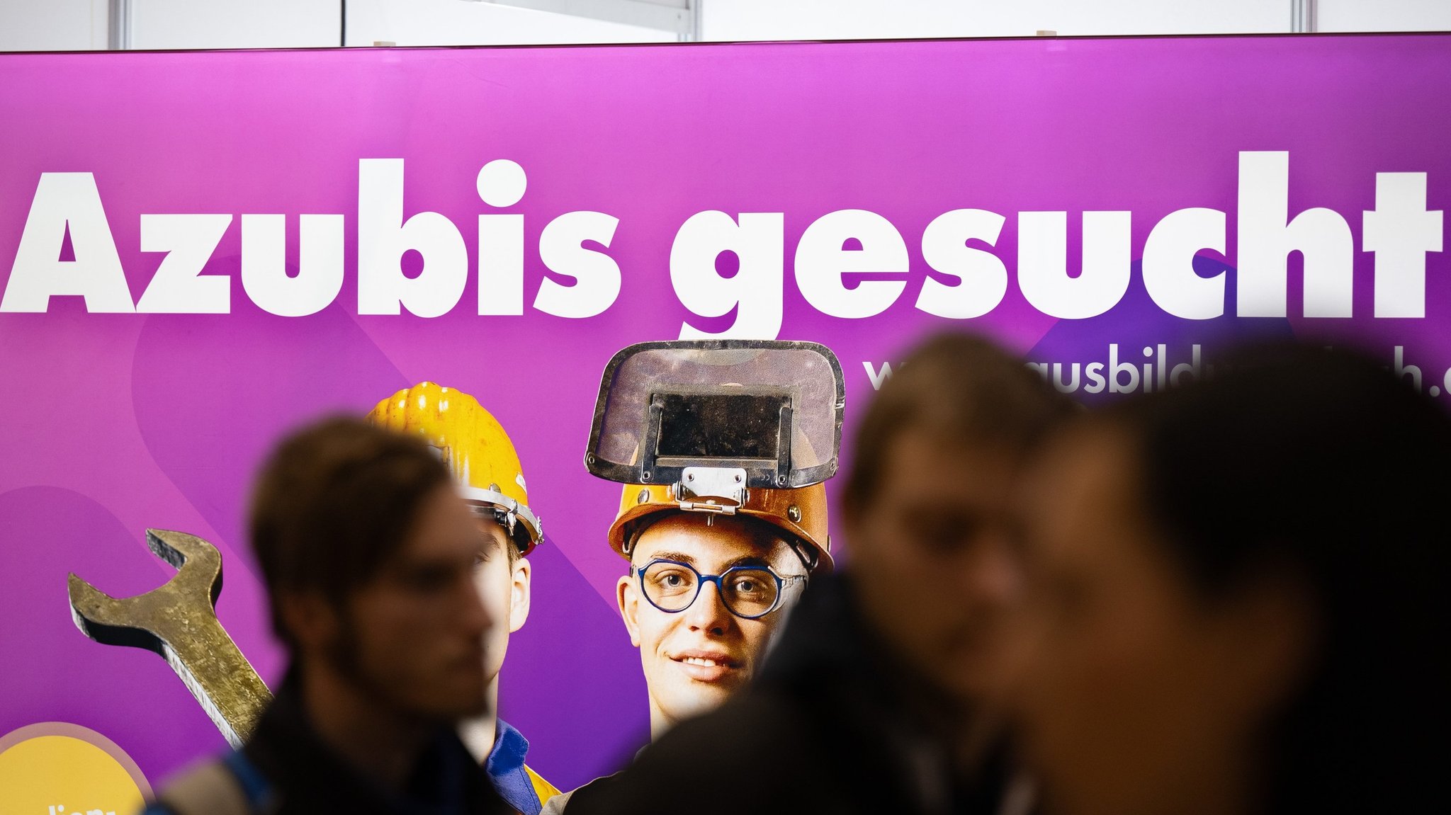 Besucher stehen auf einer Jobmesse vor einem Plakat mit dem Schriftzug "Azubis gesucht" (Symbolbild). 