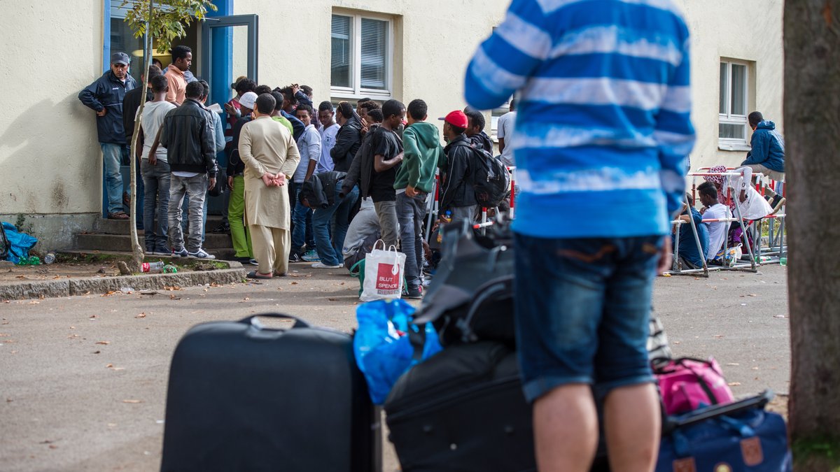 Mehrere Flüchtlinge stehen in Bayern mit ihren Koffern vor einer Erstaufnahme für Asylbewerber