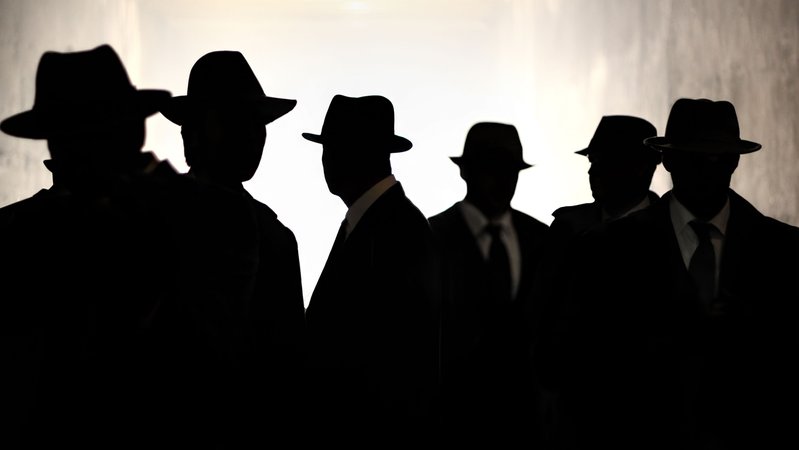Silhouetten von Männergestalten, die nicht zu erkennen sind. Sie tragen schwarze Anzüge und Hüte | Bild: stock.adobe.com/jgolby Silhouetten von Männergestalten, die nicht zu erkennen sind. Sie tragen schwarze Anzüge und Hüte