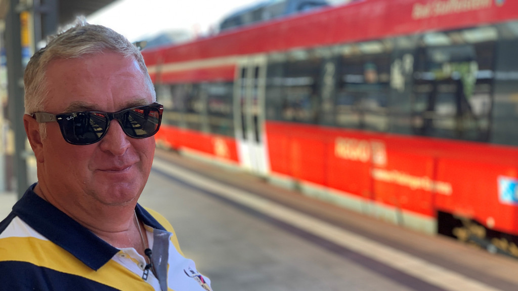 Ein Mann mit Sonnenbrille an einem Bahnhof.