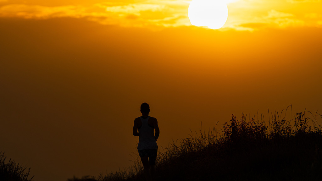 Eine joggende Person läuft auf einem Feldweg bei Frankfurt am Main dem Sonnenaufgang entgegen (Symbolbild) 