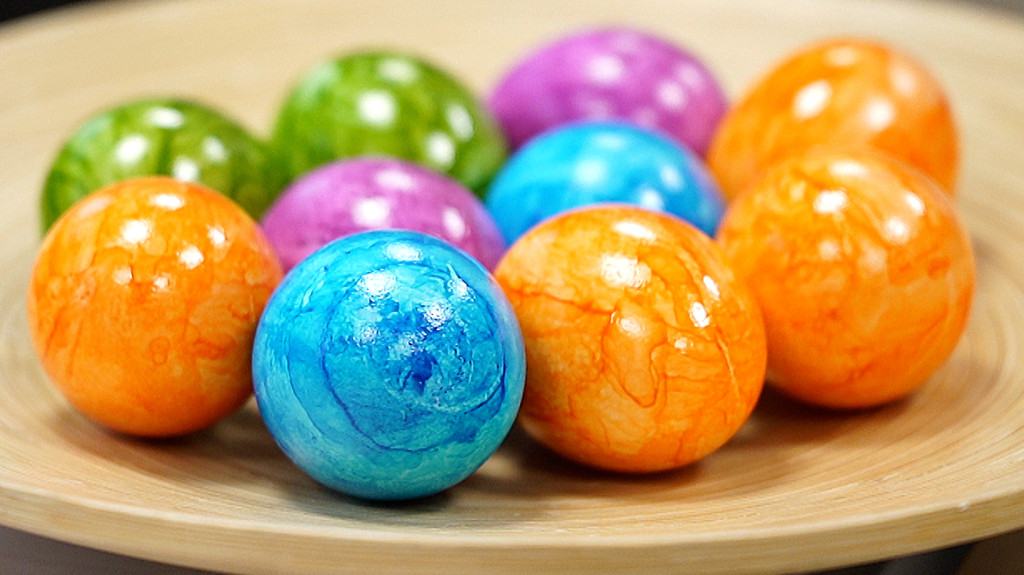 Orange, blau, rosa und grün gefärbte Eier liegen auf einer Holzschale