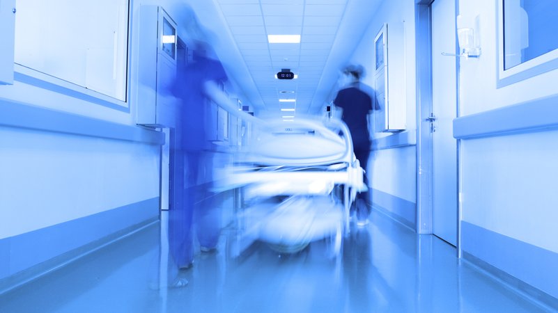 Ein Krankenbett wird durch einen Gang im Krankenhaus geschoben.