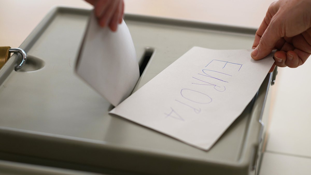Ein Wahlzettel wird in eine Wahlurne geworfen. 