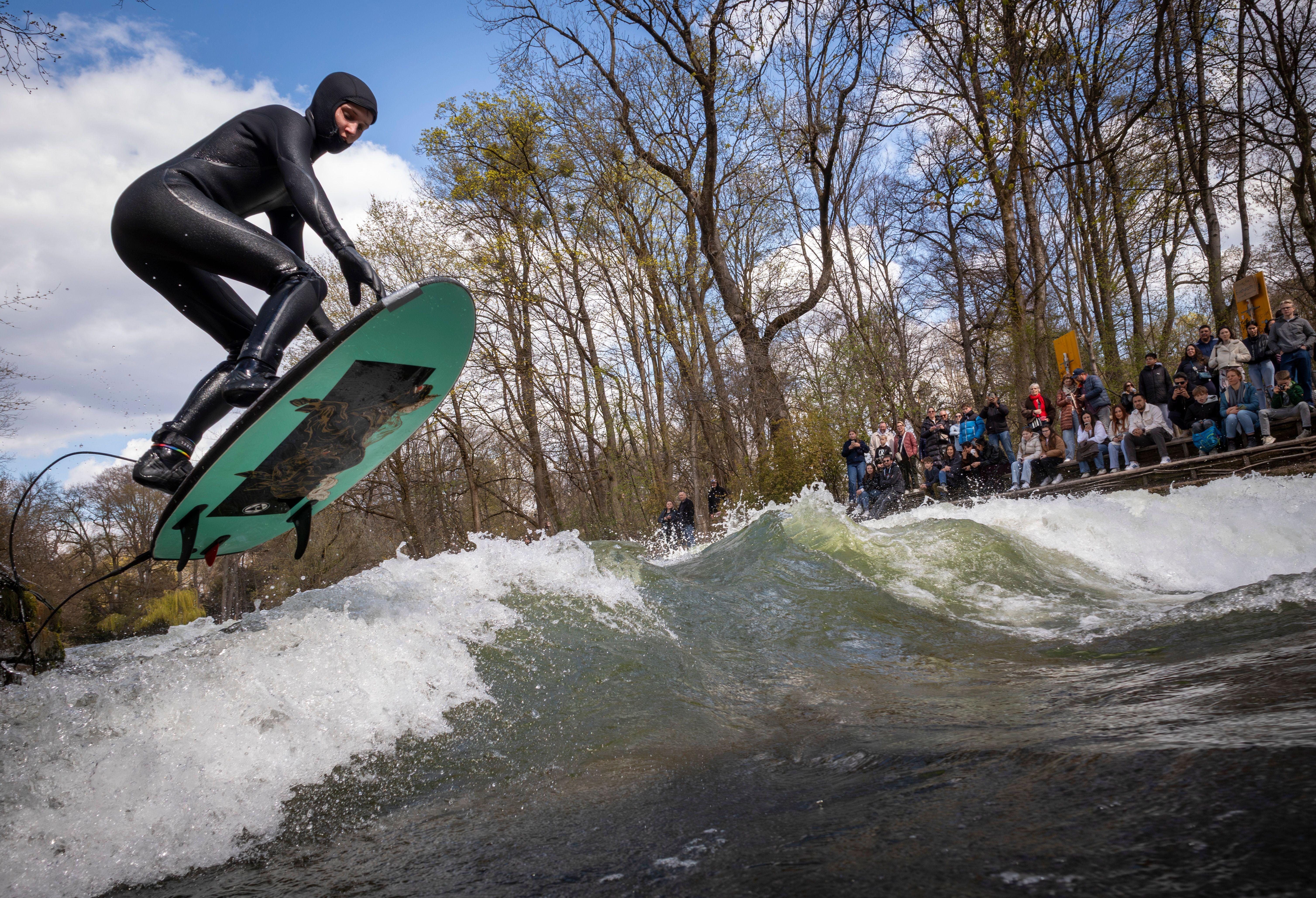 03.04.2026, Bayern, München: Ein Mann versucht mit einem großen Sprung auf die Eisbachwelle im Englischen Garten zu springen. 