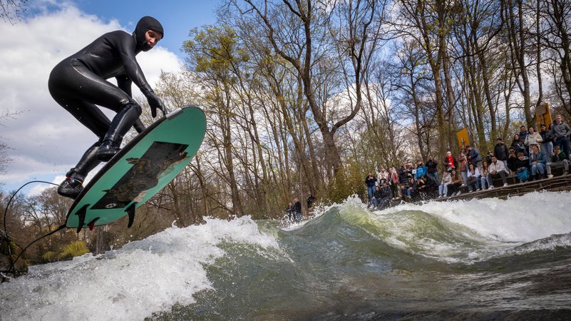 03.04.2026, Bayern, München: Ein Mann versucht mit einem großen Sprung auf die Eisbachwelle im Englischen Garten zu springen. | Bild: dpa-Bildfunk/Peter Kneffel 03.04.2026, Bayern, München: Ein Mann versucht mit einem großen Sprung auf die Eisbachwelle im Englischen Garten zu springen.