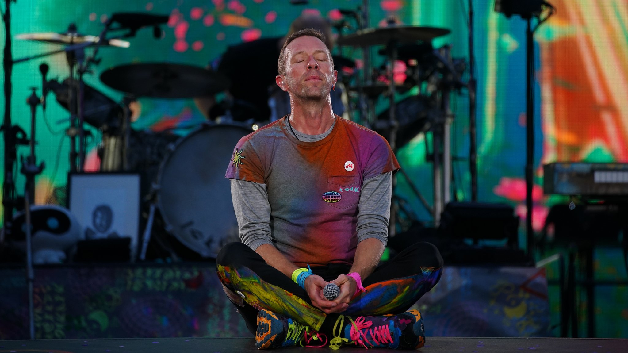 Zu sehen ist Chris Martin, Frontsänger der Band Coldplay, im Schneidersitz und geschlossenen Augen auf einer Bühne. 