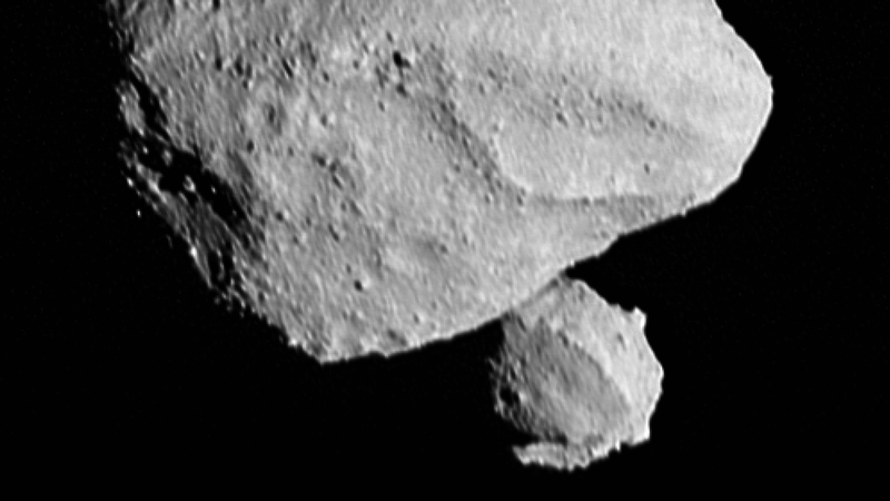 Vor einem schwarzen Hintergrund befindet sich mittig oben im Bild ein steiniger Körper: Es ist der Asteroid Dinkinesh. Rechts darunter ist eine kleinerer steiniger Körper sichtbar, der zeigt, dass der Asteroid Dinkinesh einen Mond hat. 
