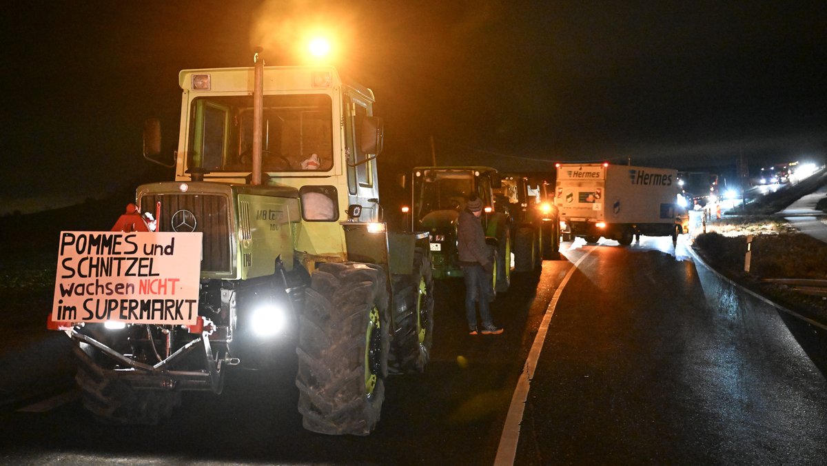 Archivbild (08.01.2024): Bei Bauernprotesten blockieren Landwirte einen Autobahnzubringer bei Rottenburg (Baden-Württemberg). Ein Traktor mit einem Banner: Pommes und Schnitzel wachsen nicht im Supermarkt.