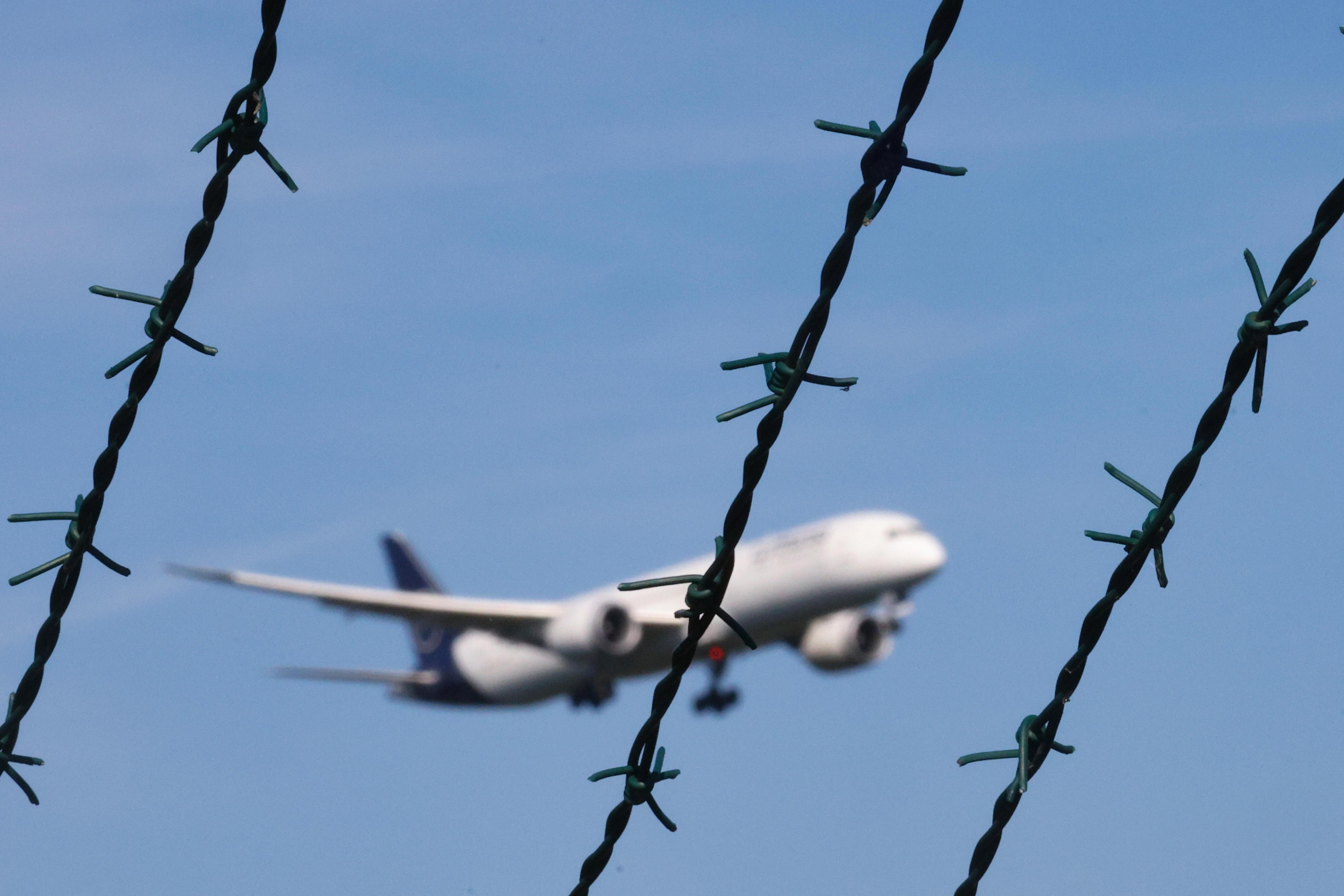Symbolbild: Ein Flugzeug im Landeanflug, im Vordergrund des Bildes ist Stacheldraht zu sehen.