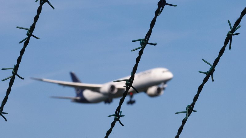 Symbolbild: Ein Flugzeug im Landeanflug, im Vordergrund des Bildes ist Stacheldraht zu sehen. | Bild: picture alliance / Rene Traut Fotografie | Rene Traut Symbolbild: Ein Flugzeug im Landeanflug, im Vordergrund des Bildes ist Stacheldraht zu sehen.