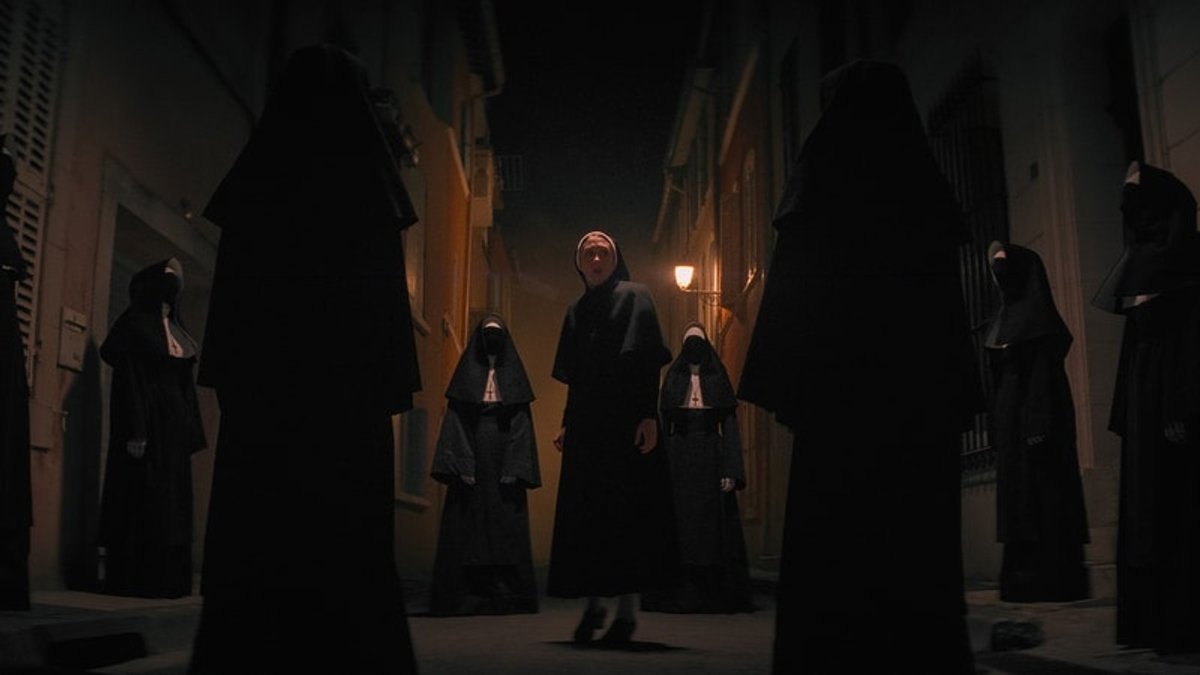 Mehrere schwarz gekleidete Nonnen umzingeln eine erscheckt blickende junge Nonne