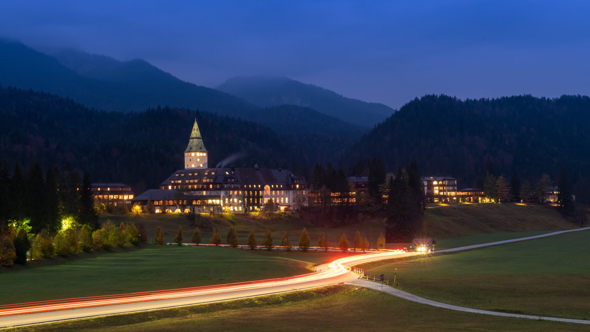 Lichterstreifen von mehreren Fahrzeugen ziehen sich auf der Zufahrtsstraße zum Schloss Elmau entlang.