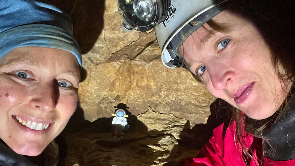 Zwei Frauen, die ein Selfie im einer Höhle machen. Eine kleine Astronautenfigur aus Plastik ist zu sehen.