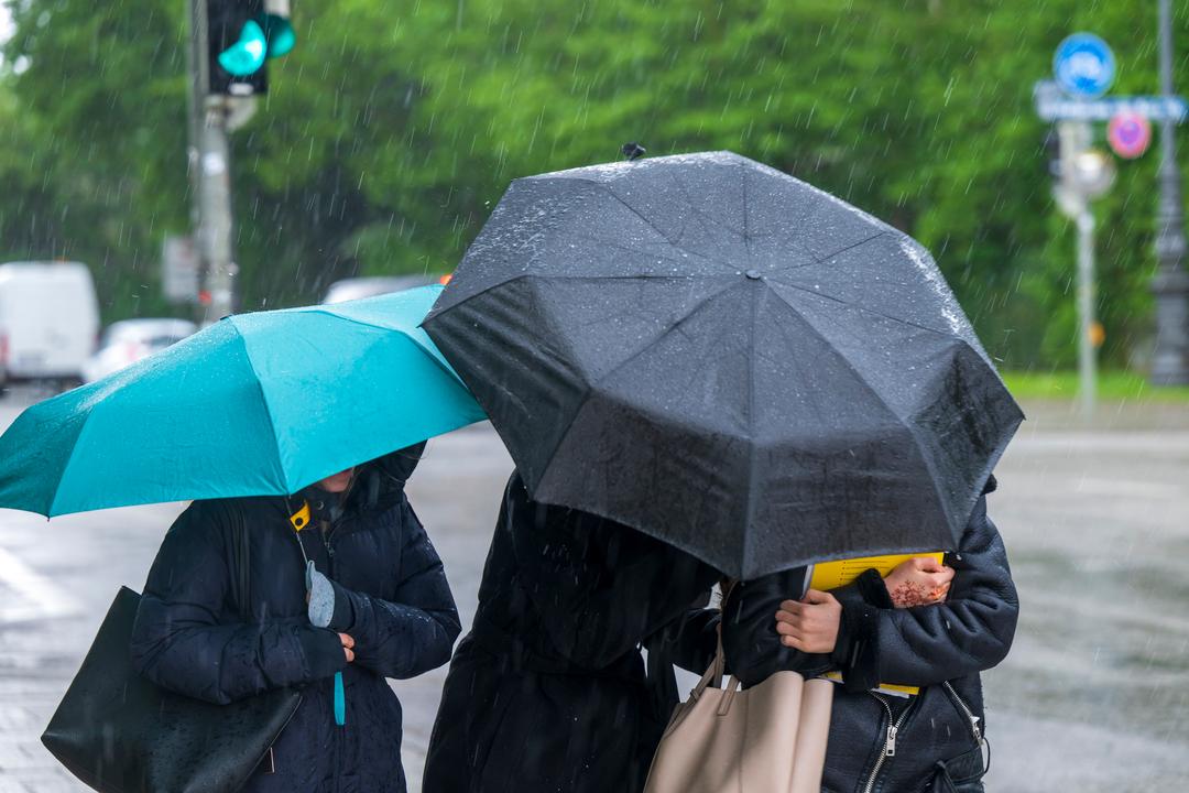München: Drei Frauen laufen bei einsetzendem Regen mit Schirmen über den Königsplatz. 
