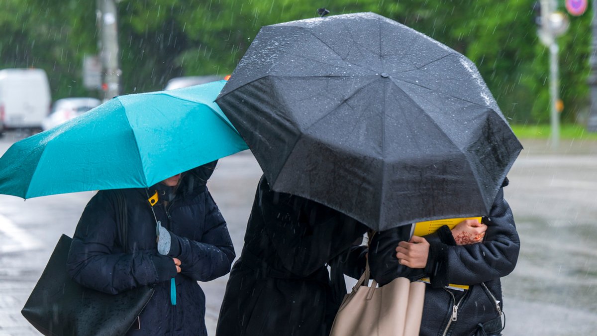 München: Drei Frauen laufen bei einsetzendem Regen mit Schirmen über den Königsplatz. 