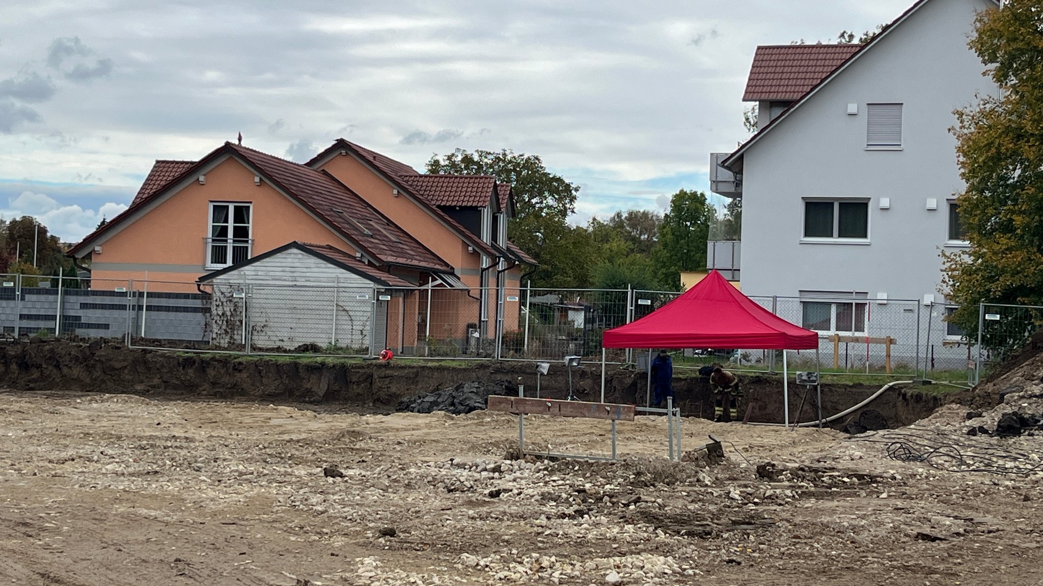 Eine Baustelle, darauf ein roter Pavillon, im Hintergrund Wohnhäuser