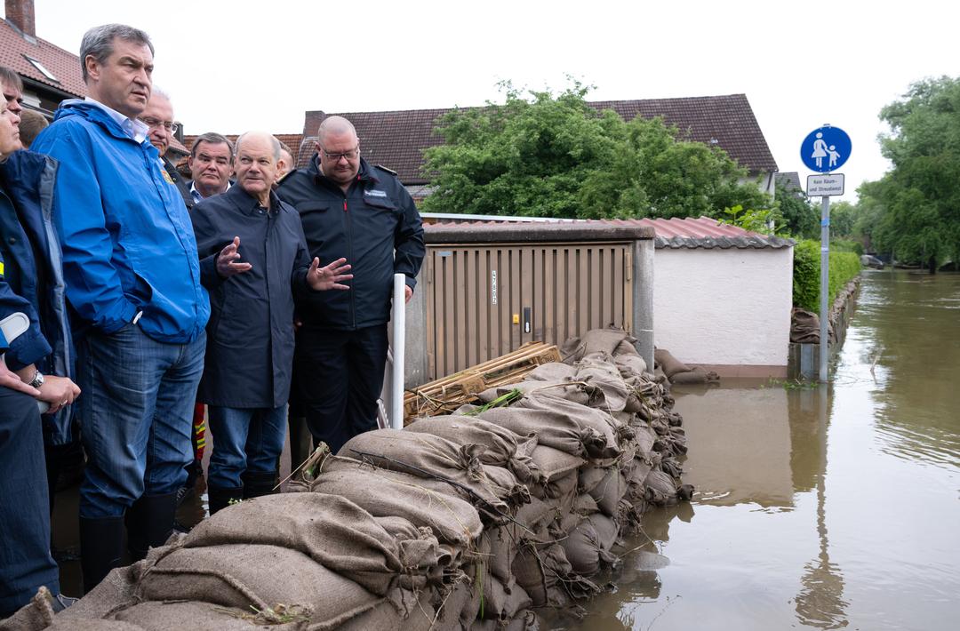 Politiker vor Sandsäcken und Hochwasser. 