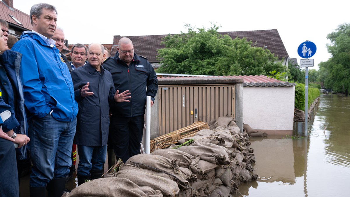 Politiker vor Sandsäcken und Hochwasser. 