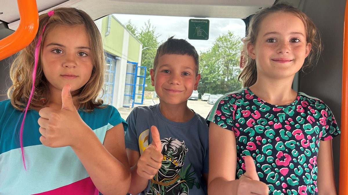 Drei Kinder zeigen den Daumen hoch in einem Bus in Passau
