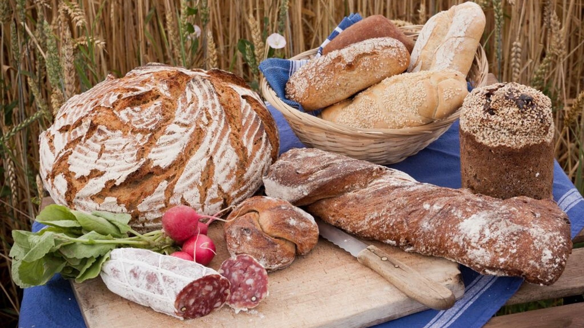 Brote, Brötchen, Wurst und Gemüse auf Holzbrett.