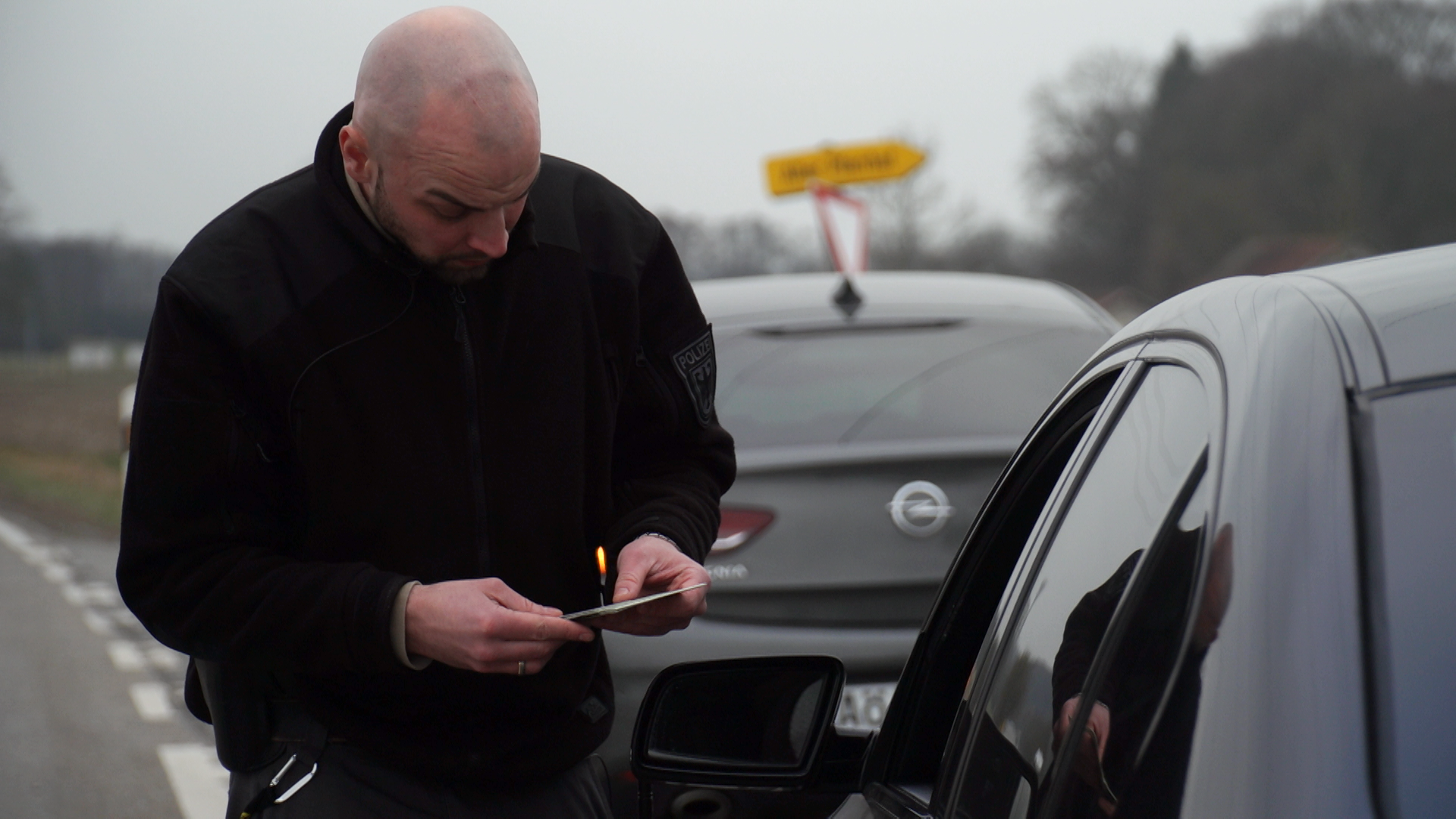 Ein Polizist kontrolliert ein Auto und lässt sich vom Fahrer die Fahrzeugpapiere zeigen.