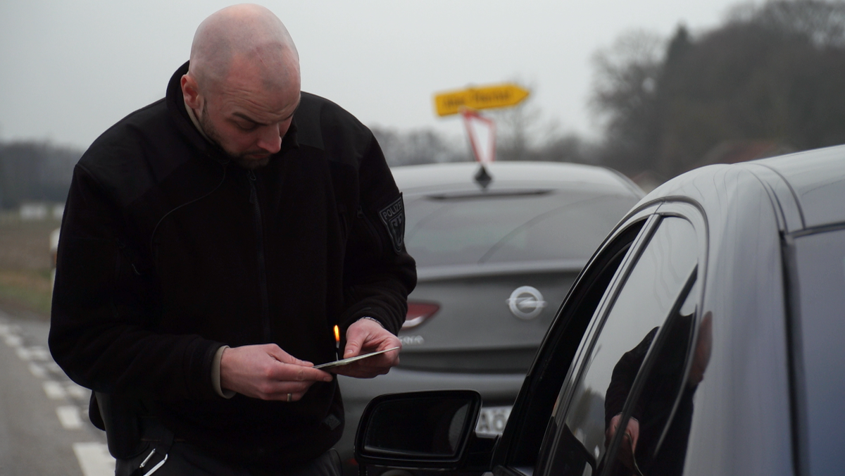 Ein Polizist kontrolliert ein Auto und lässt sich vom Fahrer die Fahrzeugpapiere zeigen.