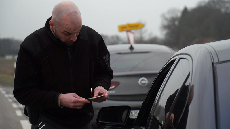 Ein Polizist kontrolliert ein Auto und lässt sich vom Fahrer die Fahrzeugpapiere zeigen.