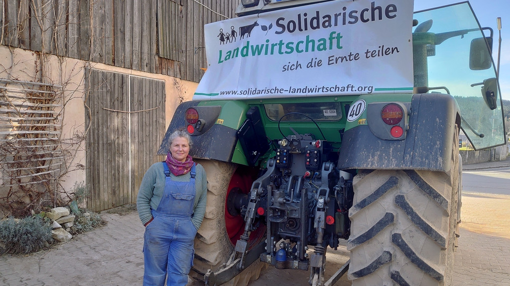 Bio-Bäuerin Claudia Dollinger steht vor ihrem Traktor und einem Banner der Solidarischen Landwirtschaft.