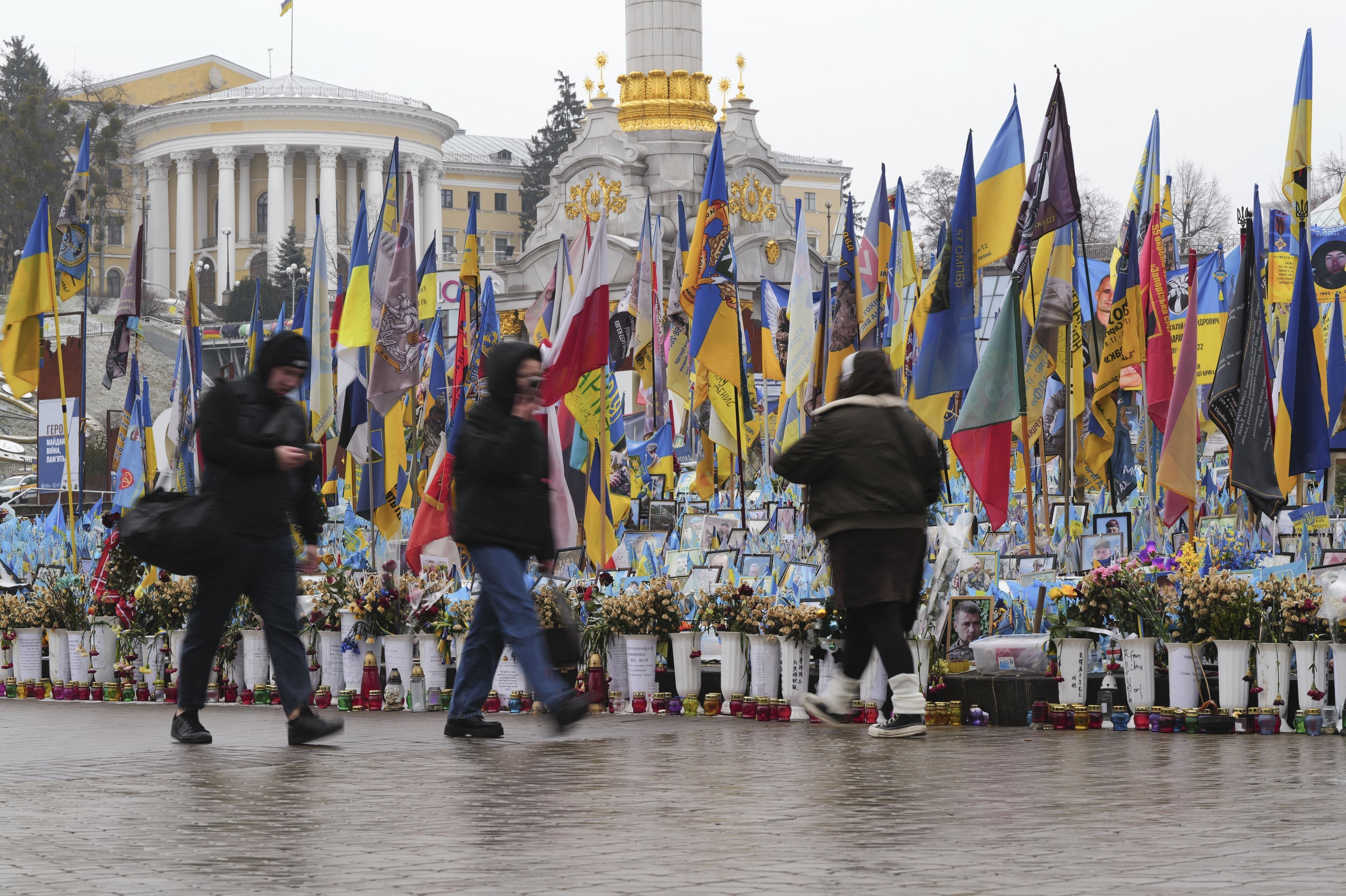 Passanten vor Blumenvasen und ukrainischen Flaggen