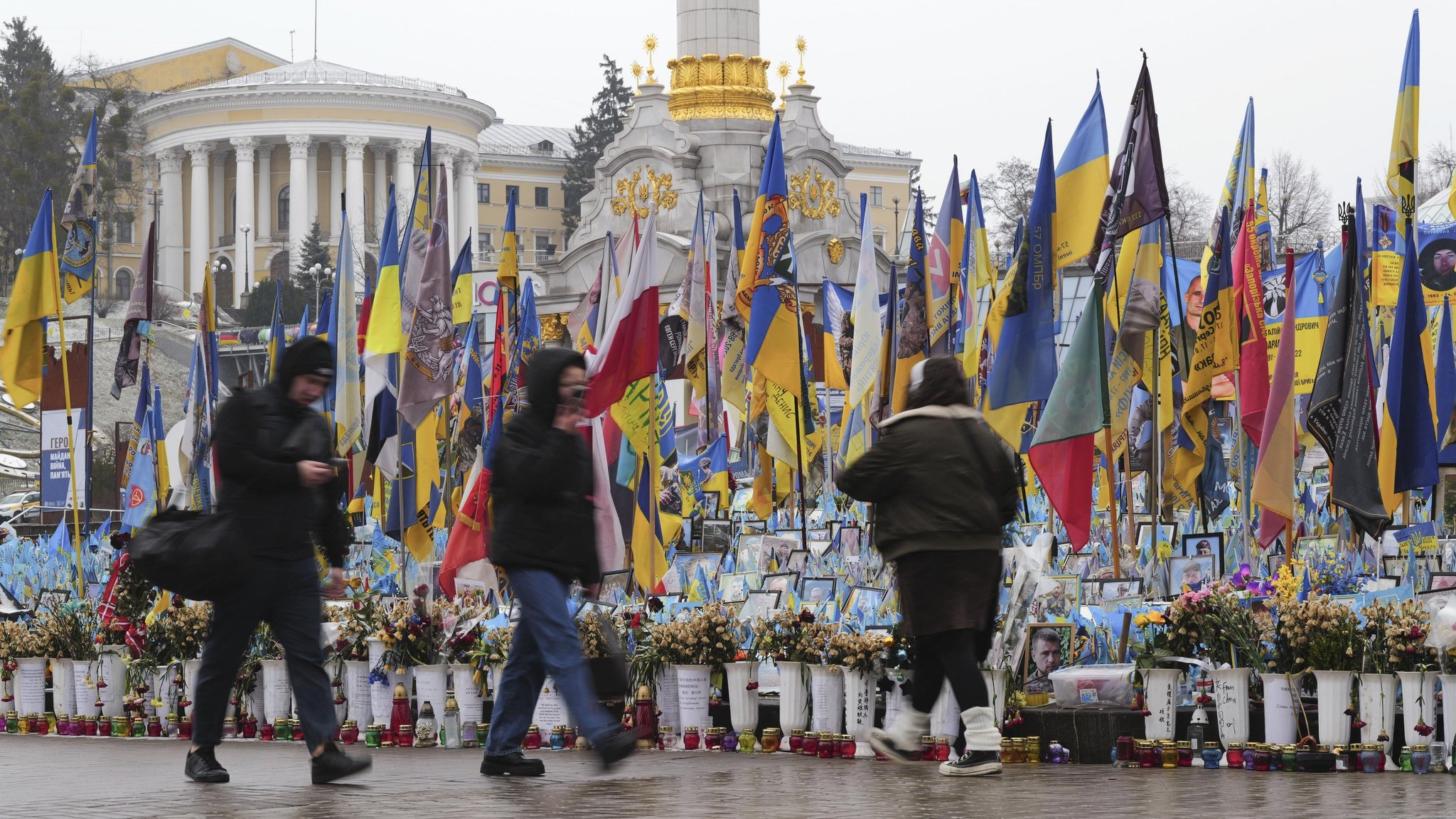 Passanten vor Blumenvasen und ukrainischen Flaggen