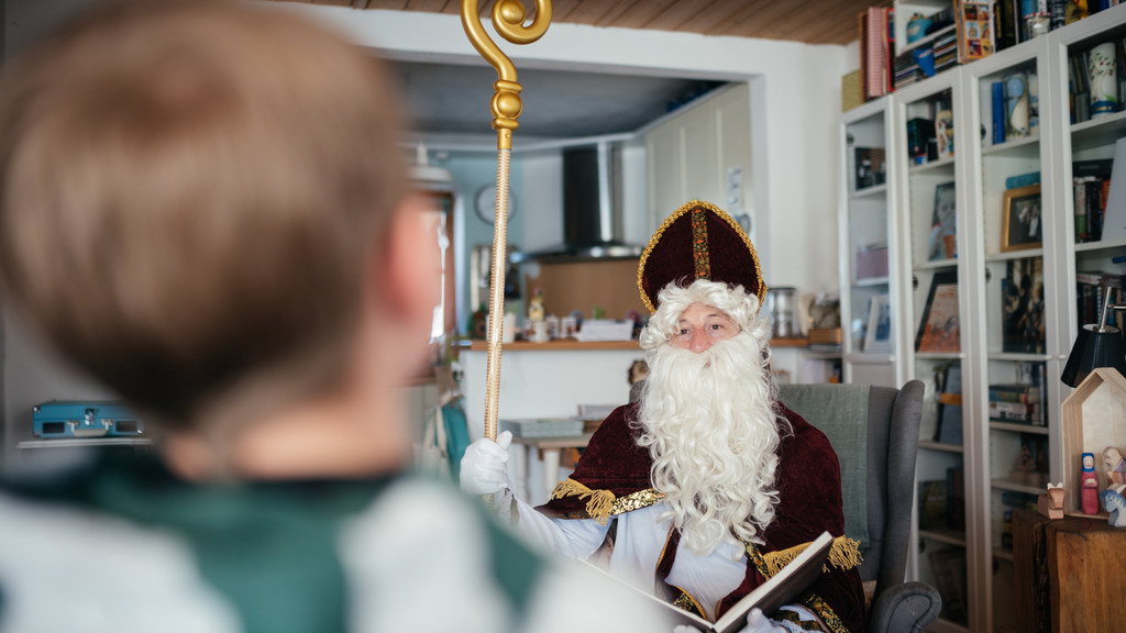 Ein Mann als Nikolaus verkleidet bei einer Familie im Wohnzimmer.